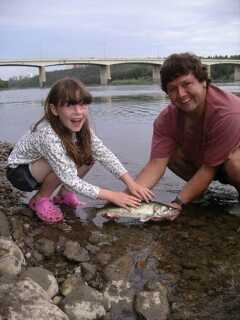 young girl and man squatting by near river stream holding small fish