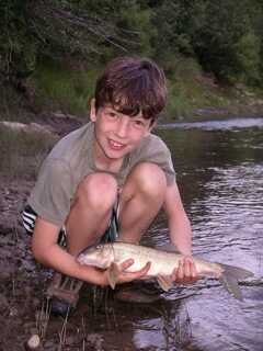 young boy squatting down and holding small fish by river stream