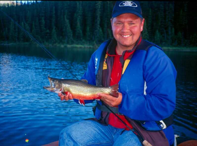 man wearing blue jacket holding brookie fish