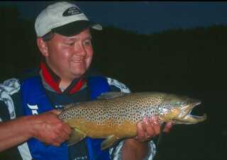 man standing in the dark looking at medium to large fish held like a bow