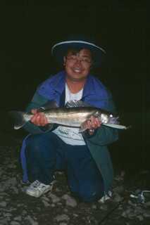 man kneeling down in the dark smiling holding medium to large fish