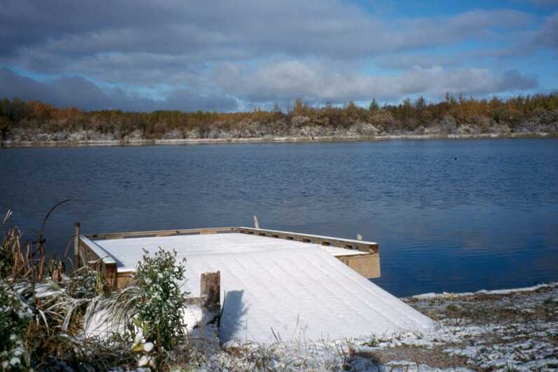 blue lake with snow covered dock winter treeline