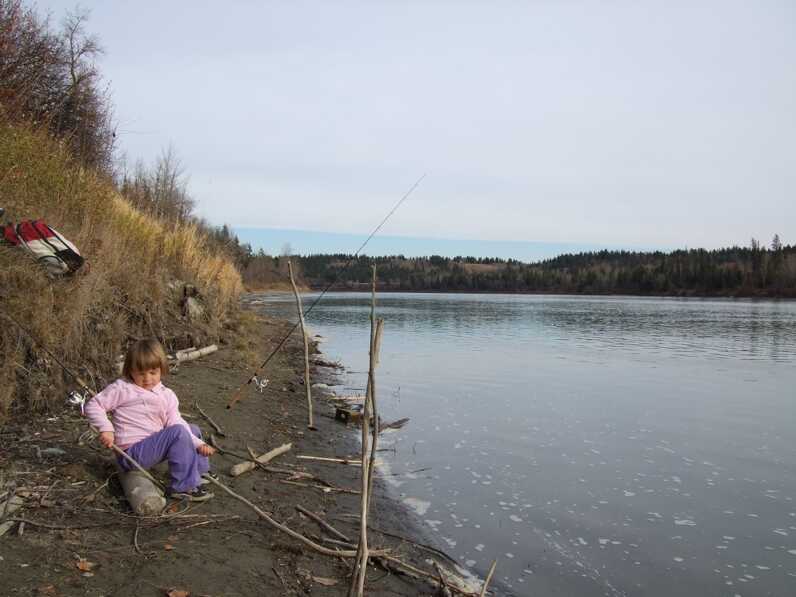 young girl sitting on ground by river stream playing with wooden stick