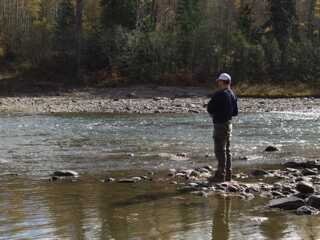 man fishing standing up on rocky river shore 