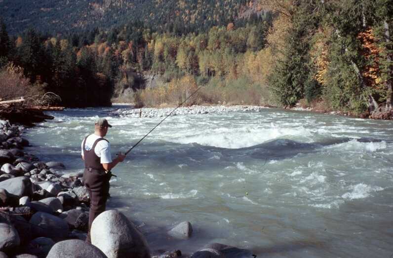 man fishing on large rocky shore of turbulent river