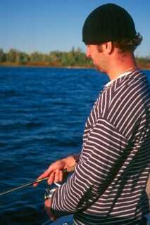 man looking down into water holding fishing rod