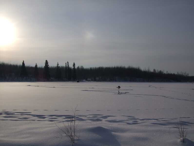 sun shines on snowy field with auger stuck in distance