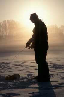 silhouette of man standing up ice fishing with bright warm sunlight behind him