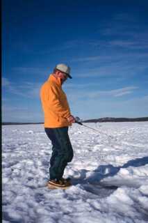 man wearing yellow jacket and jeans ice fishing in the snow