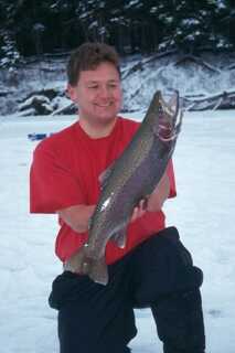 man wearing red tshirt kneeling on snow holding medium size fish