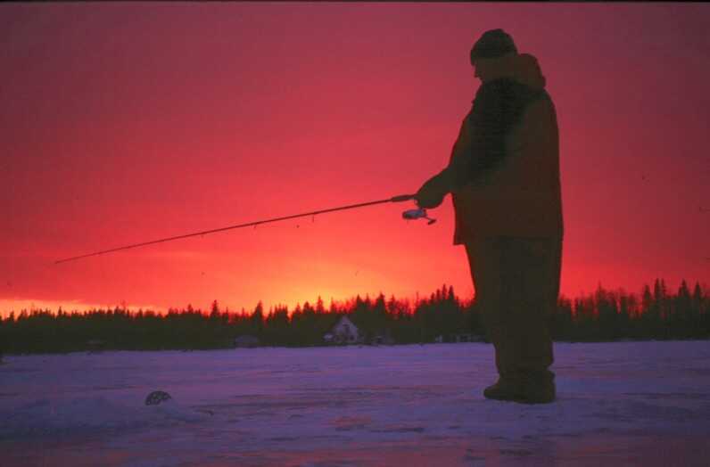 silhouette of a man ice fishing during vivid pink sunset