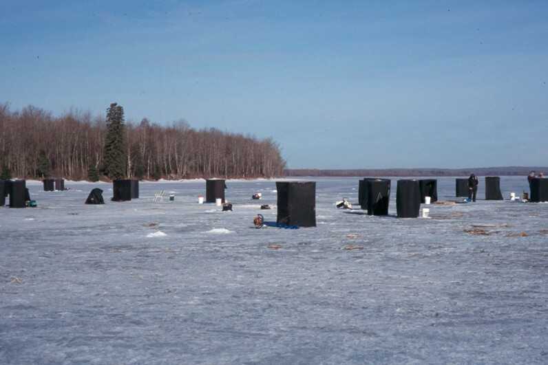 frozen lake scattered with several boxy black ice fishing tents 