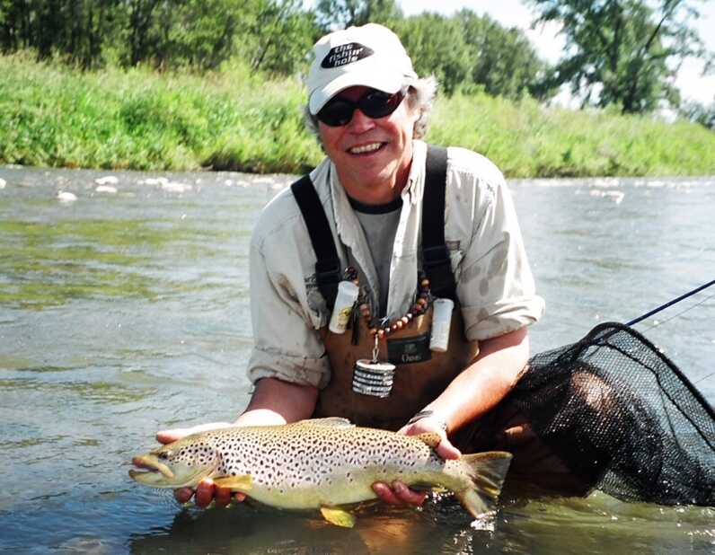 man wearing waders squats in water and holds fish next to a net