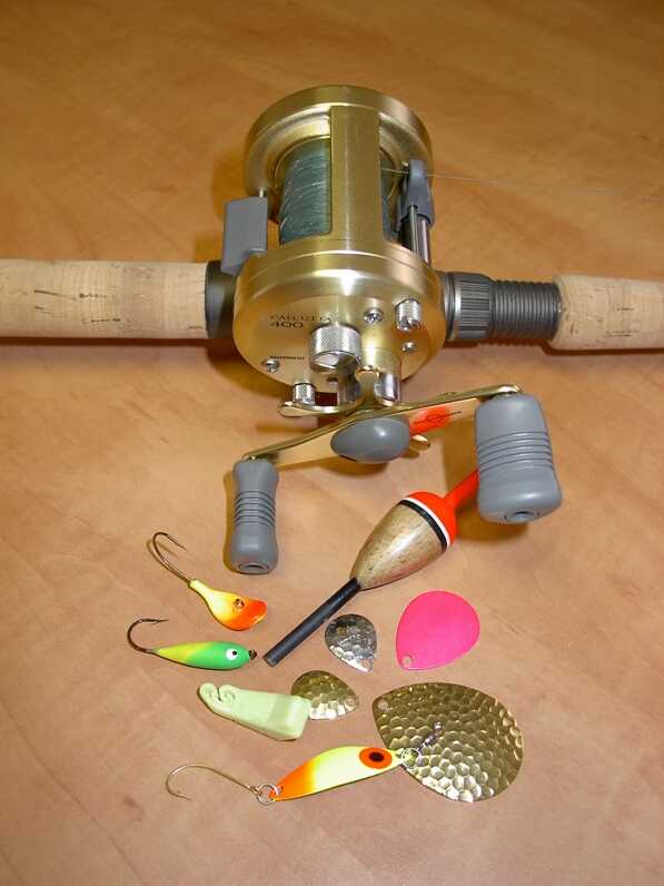 close up of reel on fishing rod and a variety of lures and bait on a wooden surface