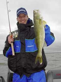 standing man holds a fishing rod in his right hand and a medium size fish with his left