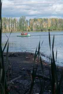 lake shore boat seen in the distance with person sitting in it during day time