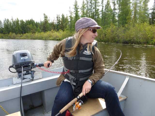 woman sitting at the end of boat holding a fishing rod handles the trolling motor