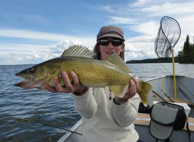 woman sitting in boat holds a walleye close to her face with both hands